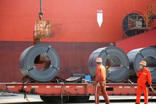 Workers load steel products for export to a cargo ship at a port in Jiangsu province