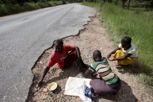 Women gather grain spilled by cargo trucks along a highway in Zimbabwe