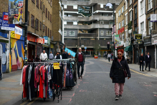 Woman walks past a clothes rail with items for sale in London