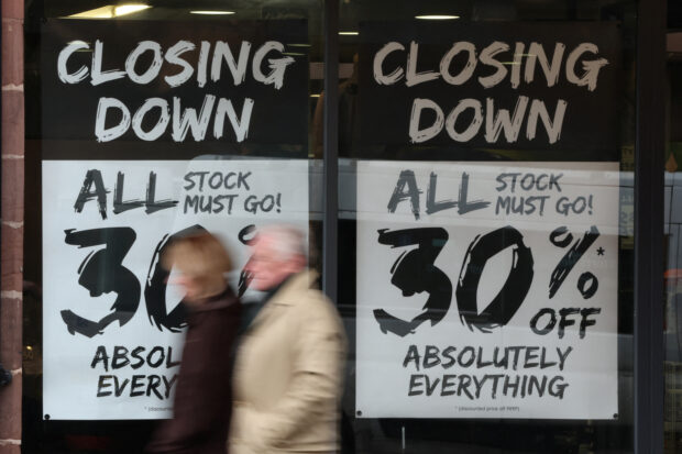 People walk past a shop with closing down signs in the window in Chester, Britain