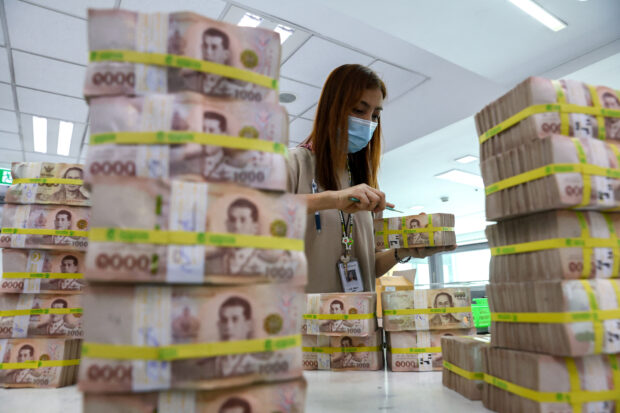 A bank employee gathers Thai baht notes at Kasikornbank in Bangkok