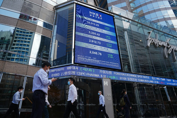 People walk past a screen displaying the Hang Seng stock index in Hong Kong