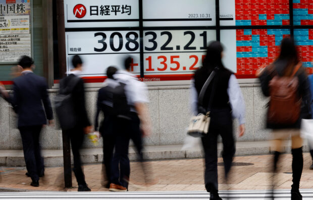 Pedestrians walk past an electronic board displaying Nikkei share average