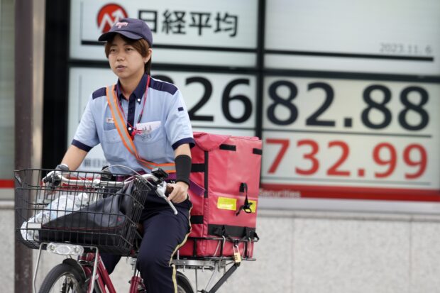 A post office worker rides a bicycle past an electronic stock board showing Japan's Nikkei 225 index in Tokyo