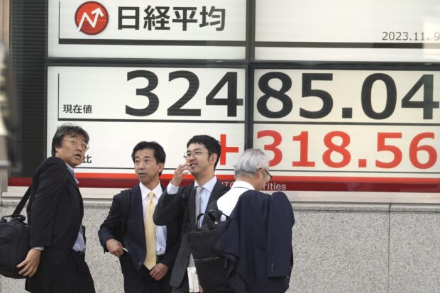 Businessmen gather in front of an electronic stock board