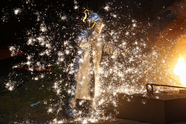 A steel worker stands amid sparks of raw iron from a blast furnace in a factory in Duisburg, western Germany