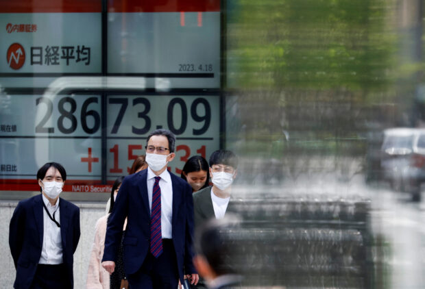 Passersby walk past an electronic stock quotation board in Tokyo