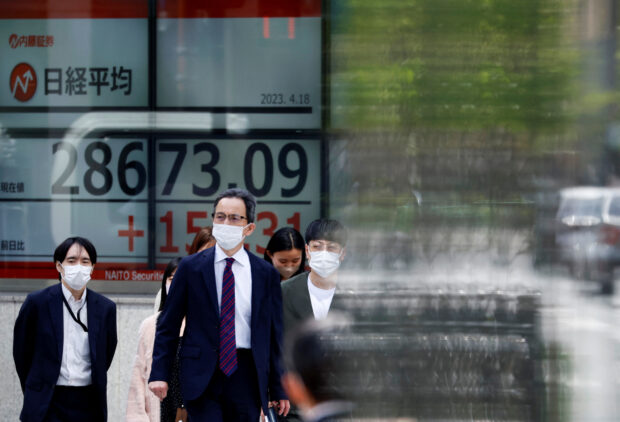 Passersby walk past an electronic stock quotation board outside a brokerage in Tokyo