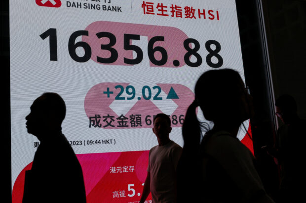 People walk past a screen displaying the Hang Seng index at central business district in Hong Kong