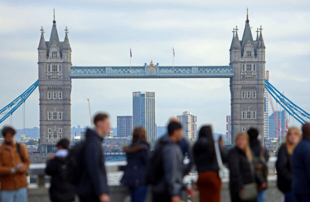 People walk over London bridge: UK pay growth slows