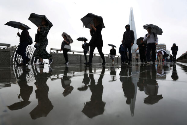 Commuters carry umbrellas while crossing London Bridge in London