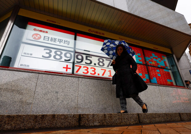 A passerby walks past in front of electronic screens displaying Japan's Nikkei share average, which surged past an all-time record high scaled in December 1989, outside a brokerage in Tokyo