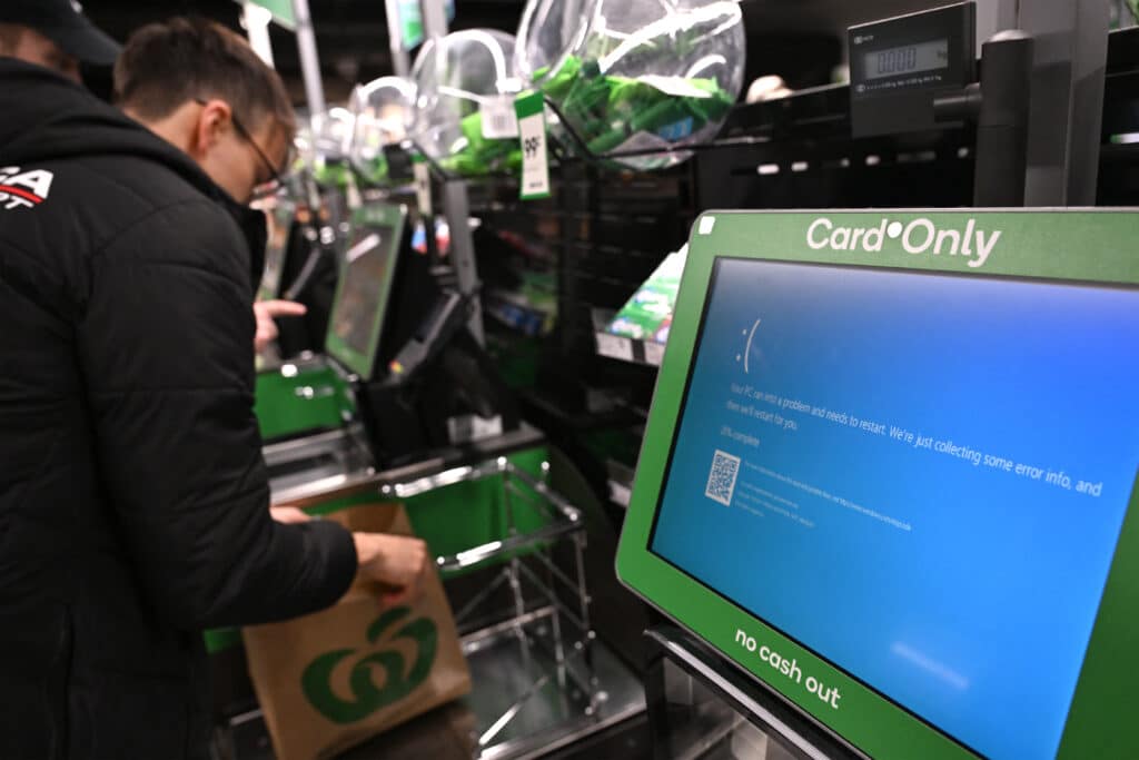 A customer takes care of his shopping next to blue screen at self-checkout terminals of a supermarket in Sydney on July 19, 2024. A large-scale outage wrought havoc on IT systems across Australia, with the country's national broadcaster, its largest international airport and a major telecommunications company reporting issues. (Photo by Saeed KHAN / AFP)