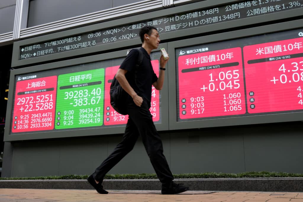 A person walks past at an electronic stock board showing financial indexes including Japan's Nikkei 225 index, green, at a securities firm in Tokyo, June 27, 2024. 