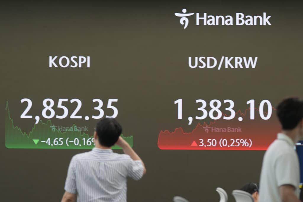 A currency trader walks near the screen showing the Korea Composite Stock Price Index (KOSPI)