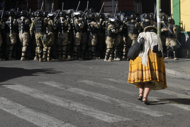 A woman walks by military police in Plaza Murillo, in La Paz, Bolivia, Wednesday, June 26, 2024.