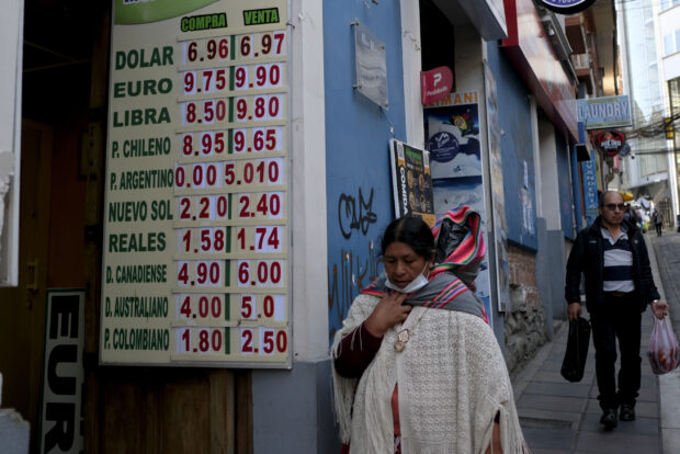 A woman walks by a sign showing the currency exchange rate in La Paz, Bolivia, Friday, June 28, 2024.