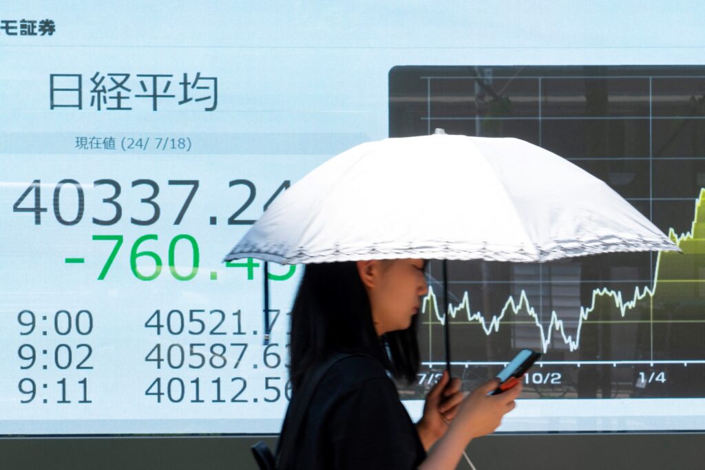 A woman walks past an electronic board displaying the numbers of the Tokyo Stock Exchange share price in Tokyo on July 18, 2024.