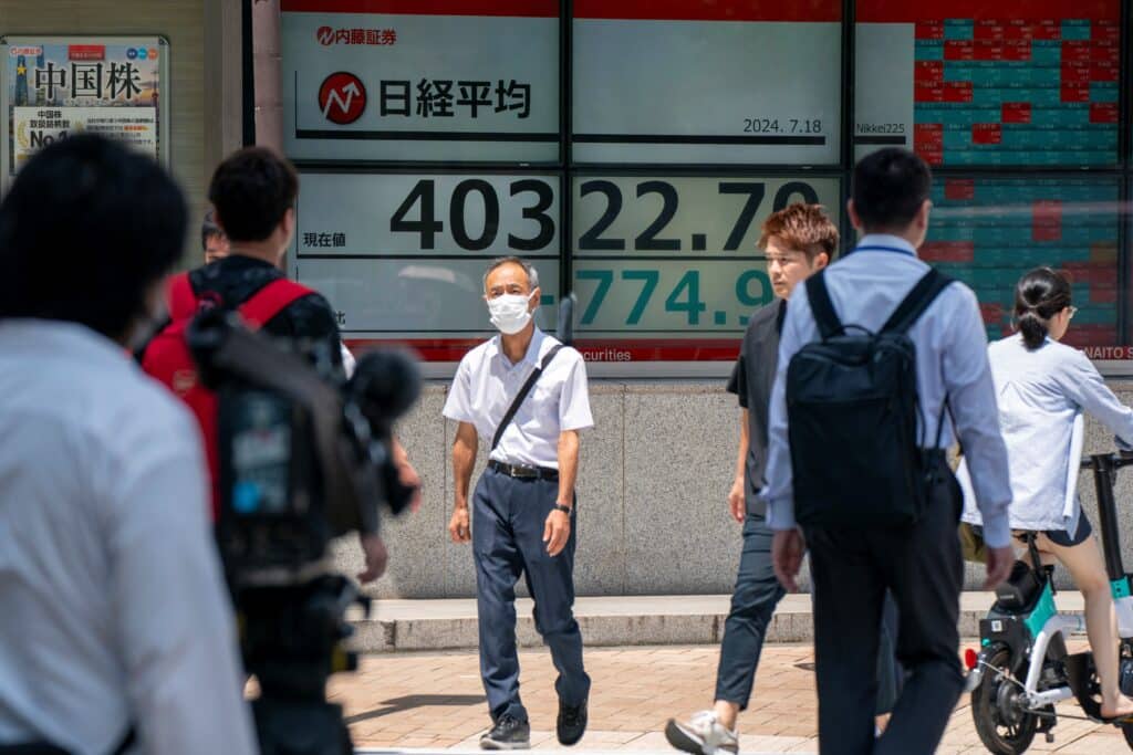 Pedestrians walk past an electronic board displaying the numbers of the Tokyo Stock Exchange share price in Tokyo on July 18, 2024. 