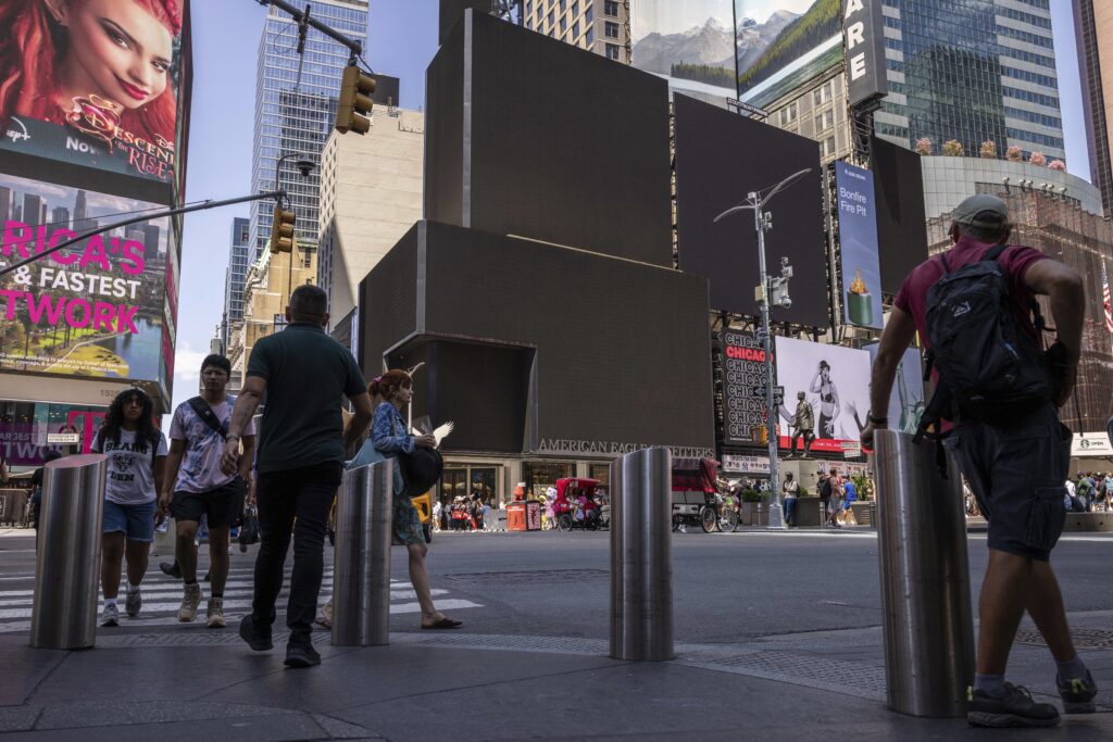 Pedestrians walk by blacked out screens, due to a global technology outage, in Times Square, Friday, July 19, 2024, in New York. 