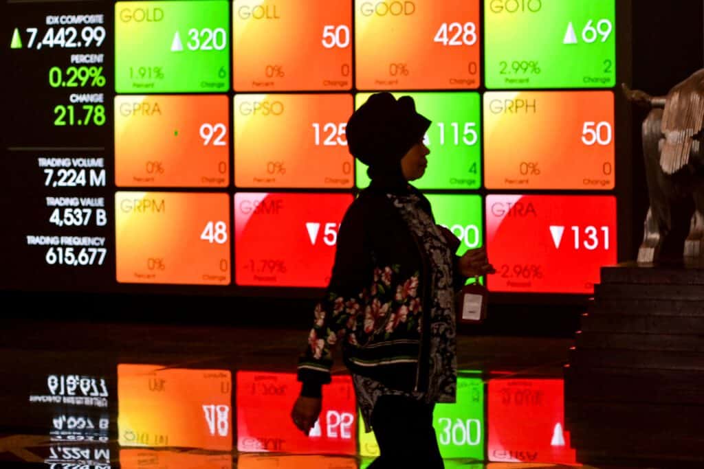 A woman walks past a large screen displaying stock indexes in Jakarta on March 14, 2024. 