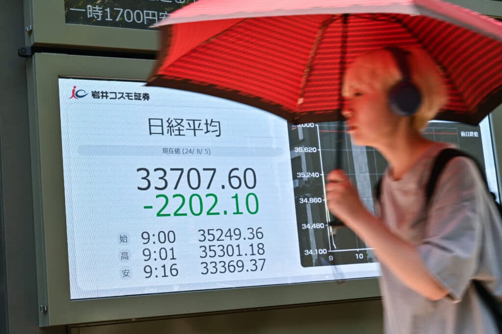 A pedestrian walks past a display board showing the morning numbers on the Tokyo Stock Exchange along a street in Tokyo on August 5, 2024. 