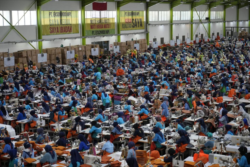 Workers sit in their stations at a factory belonging to PT Eksonindo Multi Product Industry