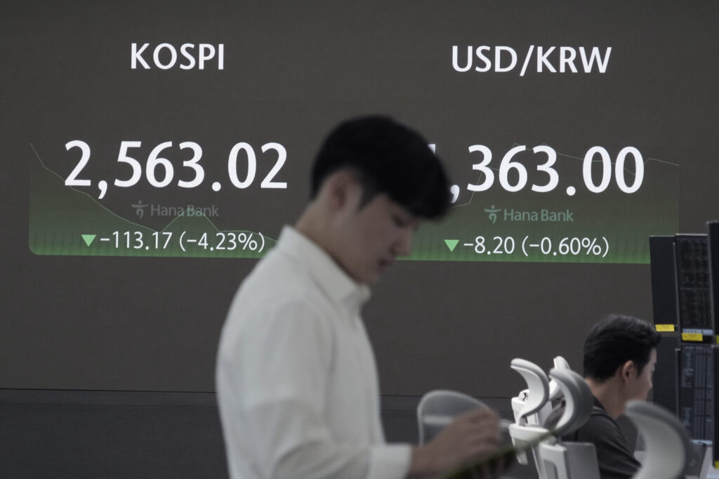 A currency trader works near a screen showing the Korea Composite Stock Price Index (KOSPI), left, and the foreign exchange rate between U.S. dollar and South Korean won at the foreign exchange dealing room of the KEB Hana Bank headquarters in Seoul, South Korea, Monday, Aug. 5, 2024. 