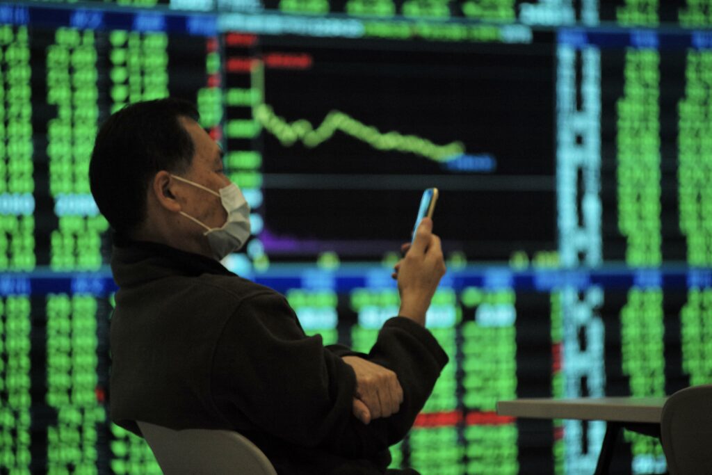 A man checks his smartphone in front of a screen showing stocks index at the Taiwan Stocks Exchange in Taipei on January 21, 2022. 