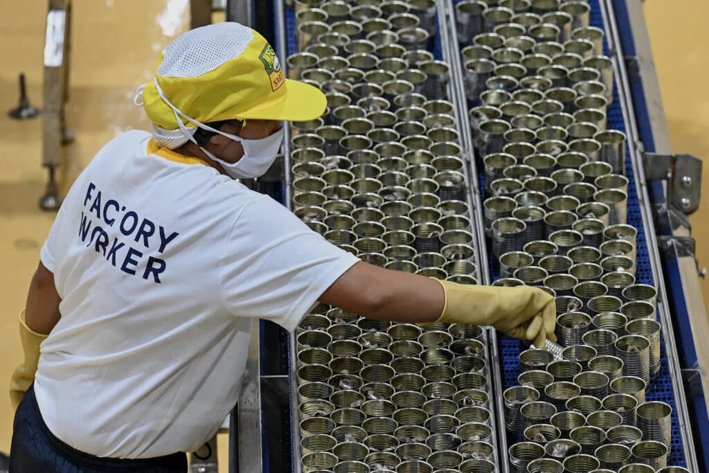 A worker arranges cans on the production line of canned sardines inside a manufacturing plant in Santo Tomas, Batangas on March 1, 2023. (Photo by JAM STA ROSA / AFP)