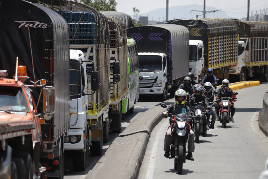 People ride motorcycles past trucks blocking a street in Bogota on September 4, 2024, during a drivers protest against the rise in the price of a subsidized gallon of diesel, which has risen by the equivalent of 46 cents on the dollar.