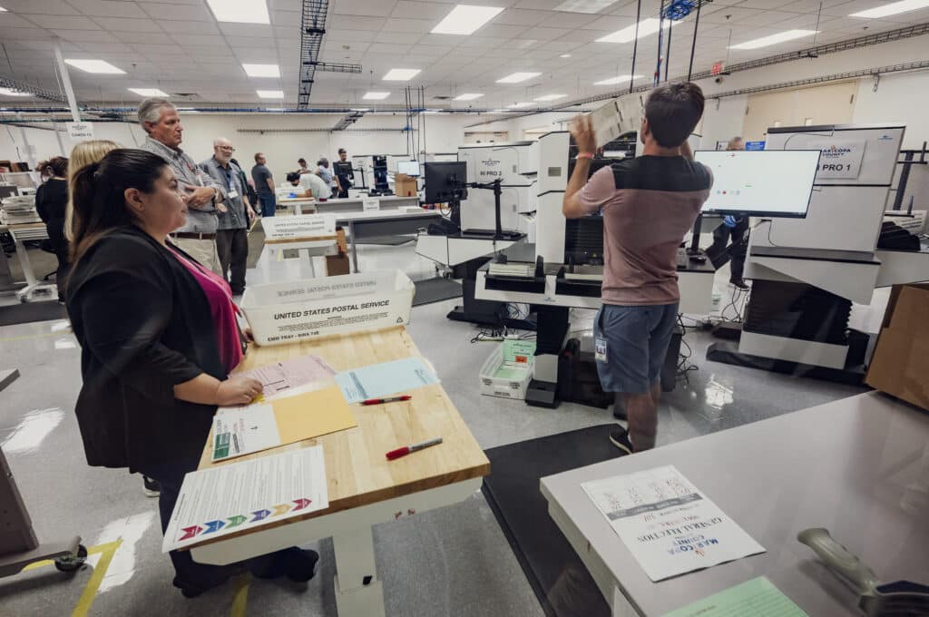 An election worker processes a stack of 2024 General Election ballots with the tabulation machine in front of observers from different parties at the Maricopa County Tabulation and Election Center (MCTEC) in Phoenix, Arizona, on October 23, 2024.