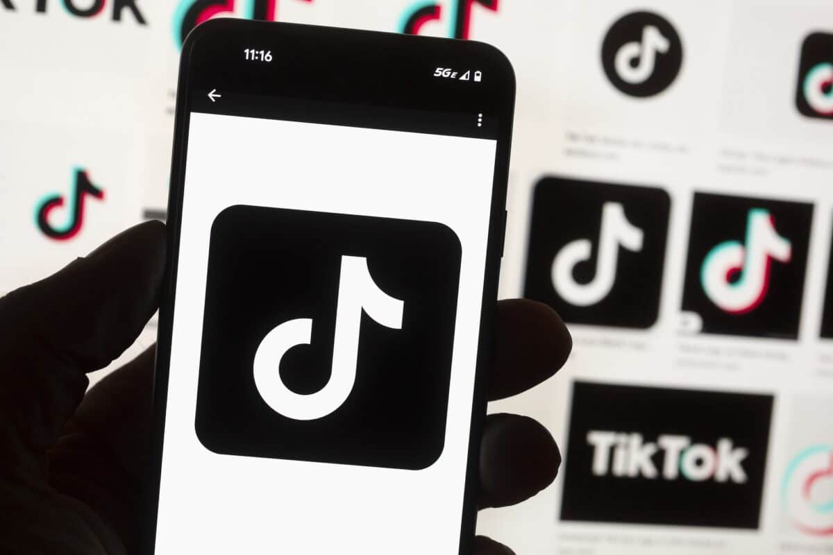 The TikTok logo is seen on a mobile phone in front of a computer screen which displays the TikTok home screen